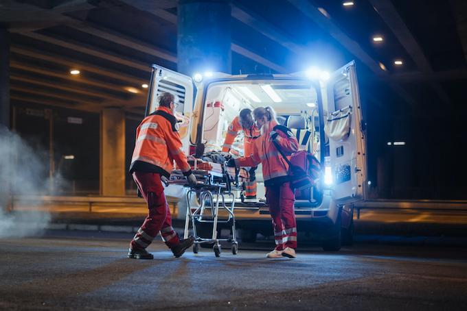 Notfallteam aus drei Personen vor Rettungswagen beim Transport einer schwerverletzten Person