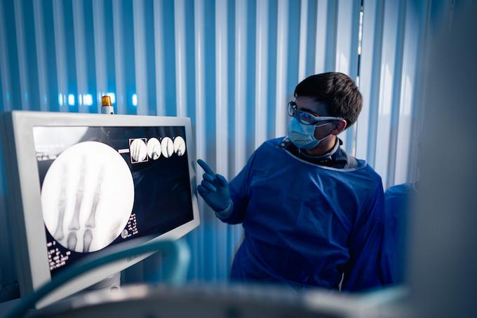 Männliche Person in OP-Kleidung zeigt auf Bildschirm mit Röntgenaufnahme